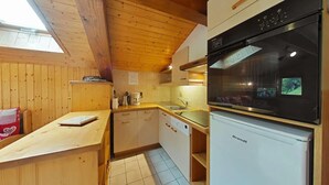 Une cuisine de taille réduite avec des murs en bois, un réfrigérateur blanc, une cuisinière et une fenêtre au-dessus de l’évier.