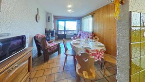 A dining area with a table set for four, wooden chairs, and a television on a wooden cabinet. - Ground floor, balcony, tv, 44m², Le Grand Bornand (Le Grand-Bornand)
