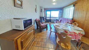 A dining area with a wooden table set for four, a television on a wooden cabinet, and a view of a balcony through a window. - Ground floor, balcony, tv, 44m², Le Grand Bornand (Le Grand-Bornand)