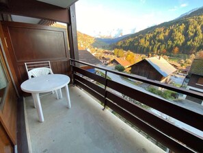 A balcony with a table and chairs, overlooking a mountainous landscape with buildings.