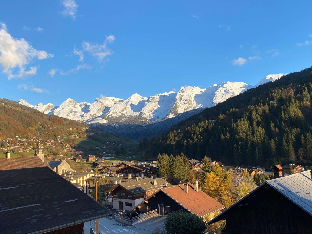 Vila montanhosa com edifícios tradicionais e vista para picos nevados.
