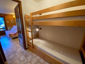 Habitación con literas de madera, un escritorio pequeño y una cama con manta estampada.