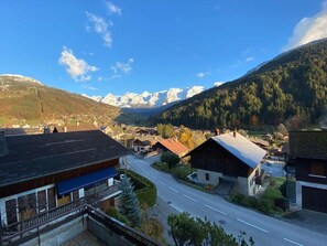 Un pueblo de montaña con edificios tradicionales, una carretera principal y montañas nevadas al fondo.