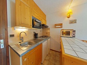 A compact kitchen with wooden cabinets, a stainless steel sink, a microwave, and a small countertop.