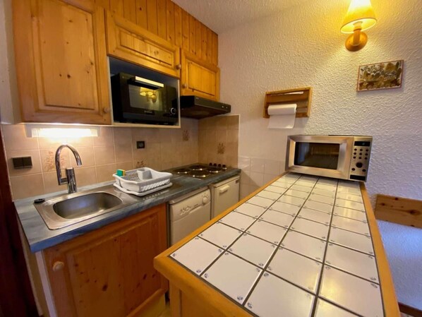 A compact kitchen with wooden cabinets, a stainless steel sink, a microwave, and a stove.