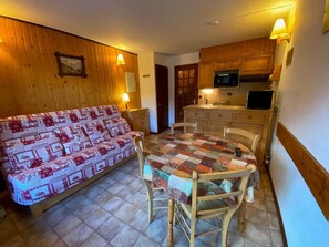 A cozy room with a wooden sofa, a quilted table, and a kitchen area with wooden cabinets and a microwave.