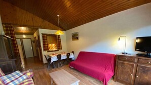 A cozy living room with a wooden ceiling, a red sofa, a wooden table, and a TV on a wooden cabinet. - 3rd floor, view mountain, balcony, tv, 41m², Le Grand Bornand (Le Grand-Bornand)