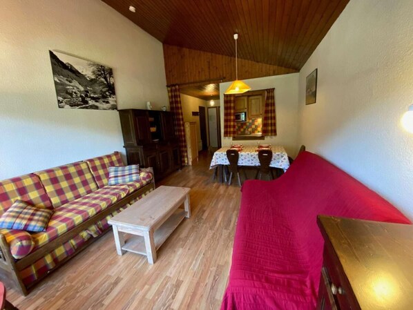 A cozy living room with a plaid sofa, a red couch, and a wooden coffee table. There is a dining area with a table and chairs, and a kitchen in the background. - 3rd floor, view mountain, balcony, tv, 41m², Le Grand Bornand (Le Grand-Bornand)