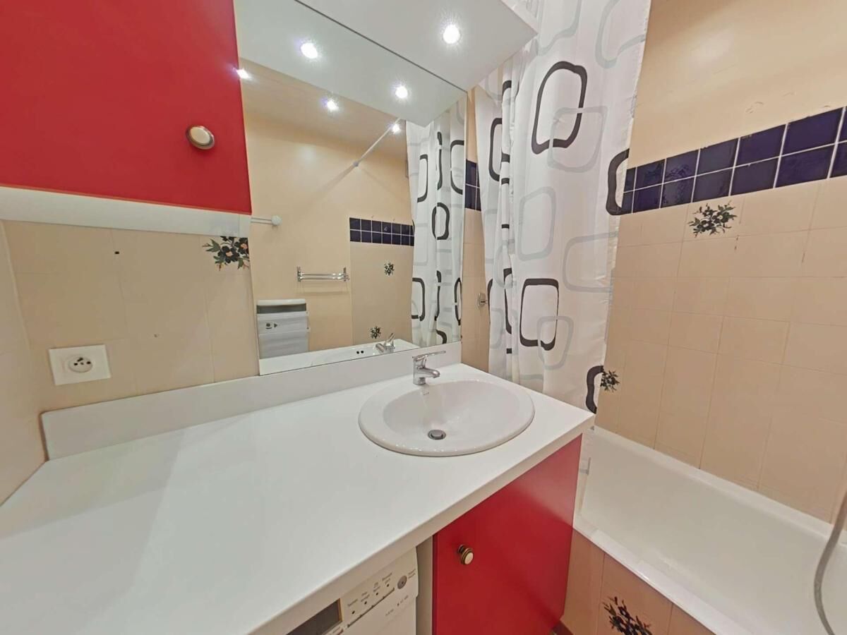 A bathroom with a white sink, red cabinet, and a mirror above it. There is a shower curtain with a geometric pattern.