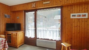 Una stanza con rivestimenti in legno, una televisione, un tavolo con tovaglia a scacchi, un termosifone e un balcone con ringhiera bianca.