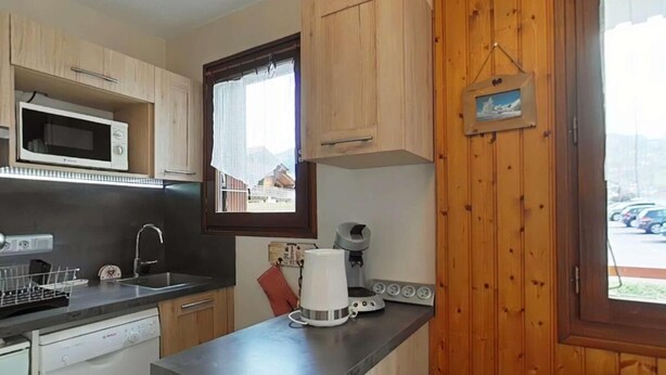 Una cucina compatta con mobili in legno, un forno a microonde, una macchina del caffè e una lavastoviglie.
