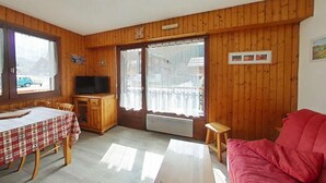 Una stanza con pannelli in legno, un tavolo da pranzo con tovaglia a quadretti, una televisione, un divano rosso e un balcone con vista.