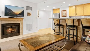 Una sala de estar moderna con chimenea, un televisor de pantalla plana y un comedor con taburetes de bar.