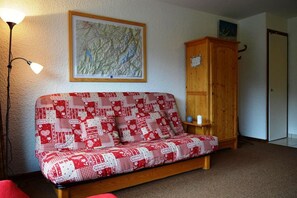 A cozy room with a red and white patterned sofa, a wooden cabinet, a map on the wall, and a lamp.