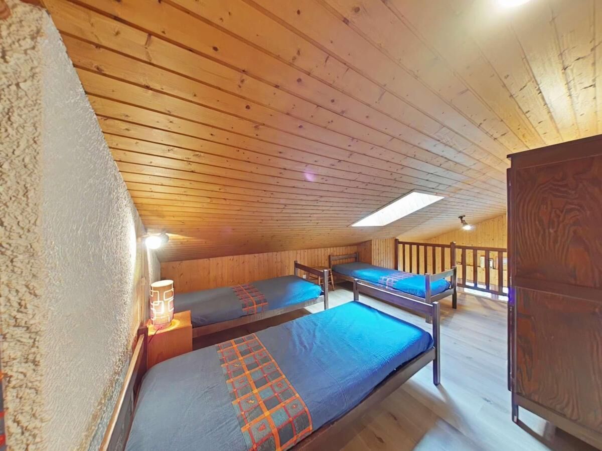 Un dormitorio con suelo y paredes de madera, dos camas individuales con ropa de cama azul, un armario de madera y un tragaluz.