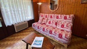 A cozy room with a wooden wall, a patterned sofa, a small table with a book, and a window with curtains. - 100m from ski slopes, Ground floor, balcony, tv, 26m², Le Grand Bornand (Le Grand-Bornand)