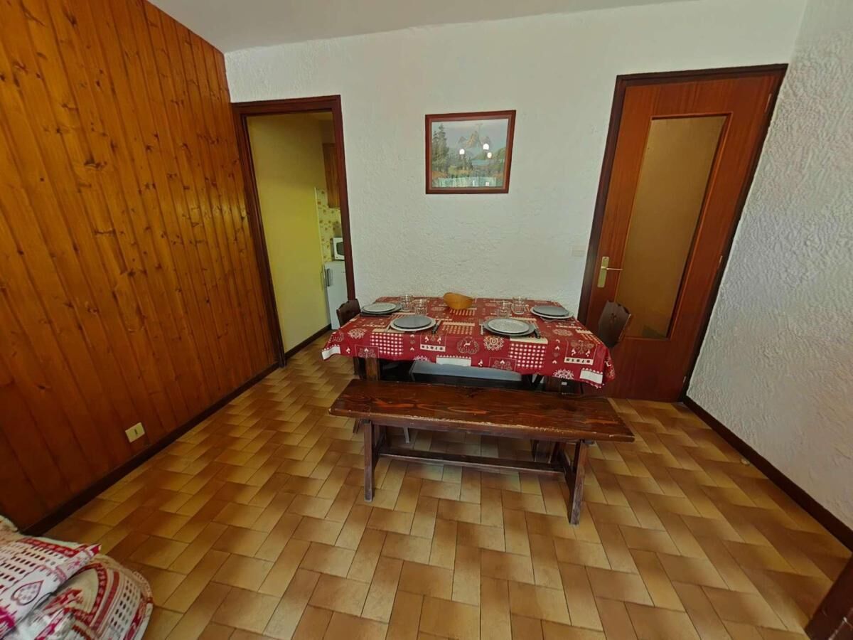Un coin repas avec une table en bois dressée pour quatre personnes, un banc et une nappe rouge à motifs.