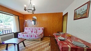 A dining area with a wooden table set for two, a sofa with a patterned cover, and a wooden floor. - 100m from ski slopes, Ground floor, balcony, tv, 26m², Le Grand Bornand (Le Grand-Bornand)