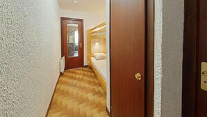 A narrow hallway with a wooden floor, a door leading to a room with a bed and a window, and a radiator on the wall. - 100m from ski slopes, Ground floor, balcony, tv, 26m², Le Grand Bornand (Le Grand-Bornand)