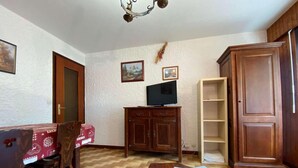 A room with a wooden dining table, chairs, a television on a cabinet, and a bookshelf. - 100m from ski slopes, Ground floor, balcony, tv, 26m², Le Grand Bornand (Le Grand-Bornand)