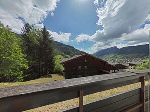 Une cabane en bois dotée d’un balcon, entourée d’une végétation luxuriante et avec des montagnes en toile de fond.