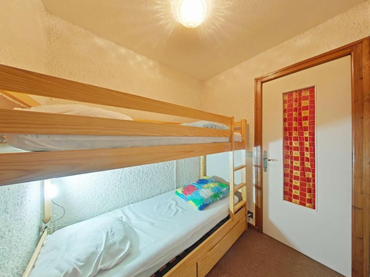 Ein Schlafraum mit Etagenbett, Holzleiter, Nachttisch und buntem Kopfkissen.