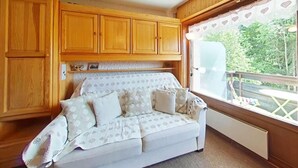 A cozy room with a white sofa, wooden cabinets, and a window with a view of greenery. - Ground floor, balcony, tv, 22m², Le Grand Bornand (Le Grand-Bornand)