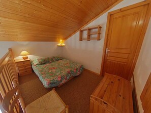 Een kleine, knusse slaapkamer met een houten plafond, een enkel bed met bloemenbeddengoed, een nachtkastje met een lamp, een houten stoel en een houten kledingkast.