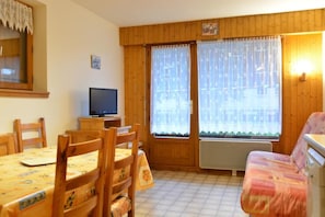 A cozy room with wooden walls, a dining table with chairs, a sofa, and a television on a small table. - 350m from resort center, Ground floor, balcony, tv, 35m², Le Grand Bornand (Le Grand-Bornand)