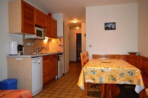 A compact kitchen with wooden cabinets, a microwave, a sink, and a dishwasher. There is a dining table with chairs and a tablecloth. - 350m from resort center, Ground floor, balcony, tv, 35m², Le Grand Bornand (Le Grand-Bornand)