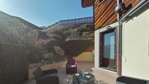 An outdoor patio with wicker furniture, a patterned rug, and a view of a hillside.