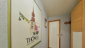 A hallway with a framed poster of Thônes, Haute Savoie, France, a wooden door, and a small framed picture on the wall.