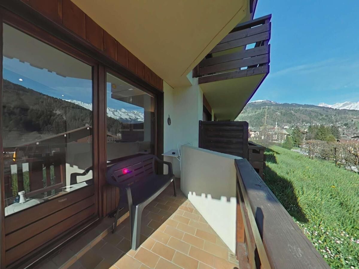 A balcony with a view of snow-capped mountains, a wooden deck, and a small table with a chair.