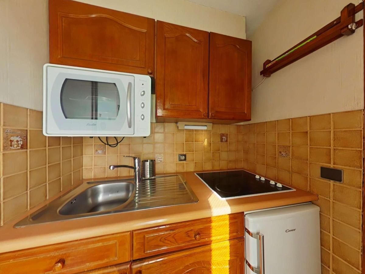 Une cuisine compacte avec des meubles en bois, un four à micro-ondes, un évier, une cuisinière et un petit réfrigérateur.