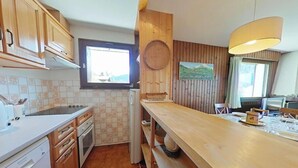A compact kitchen with wooden cabinets, a built-in oven, and a window overlooking a scenic landscape. - Floor -1, view mountain, balcony, fireplace or stove, tv, 56m², Le Grand Bornand (Le Grand-Bornand)