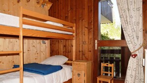 A wooden cabin room with bunk beds, a small wooden chair, a nightstand, and a window with curtains. - Floor -1, view mountain, balcony, fireplace or stove, tv, 56m², Le Grand Bornand (Le Grand-Bornand)