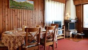 A dining area with wooden walls, a painting of a landscape, a fireplace, and a television. - Floor -1, view mountain, balcony, fireplace or stove, tv, 56m², Le Grand Bornand (Le Grand-Bornand)