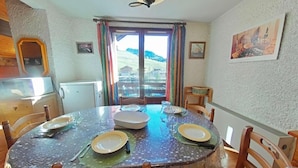 Un comedor con una mesa redonda dispuesta para cuatro personas, sillas, una ventana con cortinas y vistas a un paisaje montañoso.