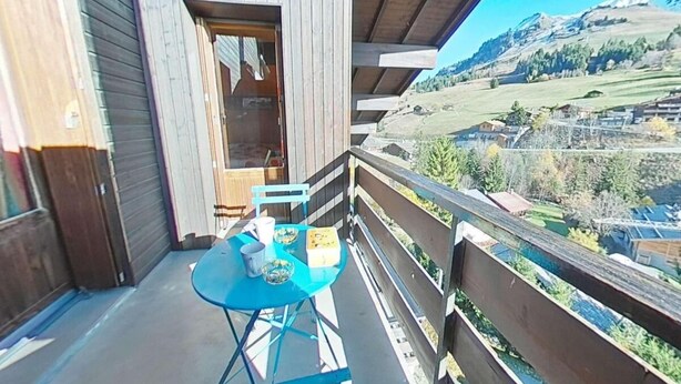 Un balcón con mesa y sillas, con vistas a un paisaje montañoso.