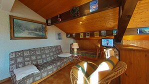 Un interior de cabaña acogedor con un sofá, una mesita, una lámpara y un televisor.