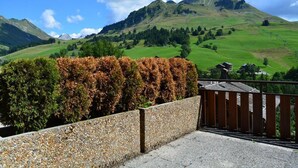 Une vue panoramique d’un paysage montagneux, avec un mur de pierre et une clôture en bois au premier plan.