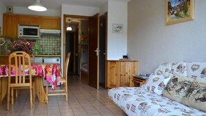 Un salon confortable avec un canapé et une table à manger entourée de chaises. Il y a également un coin cuisine avec des placards en bois et un four à micro-ondes.
