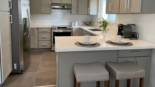 Una cocina moderna con armarios grises, electrodomésticos de acero inoxidable, una isla central con taburetes y una cafetera.