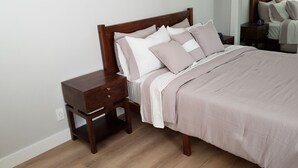 Una cama bien hecha con cabecera de madera, una mesita de noche con cajón y una pequeña mesita auxiliar.