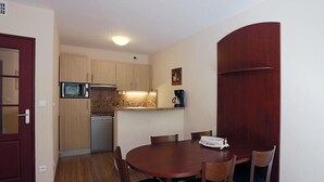 A compact kitchen with a microwave, coffee maker, and wooden cabinets. There is a dining table with chairs and a red door. - 100m from ski slopes, 1st floor, jacuzzi, hammam, parking, tv, ski locker, 41m², Peyragudes (Germ)
