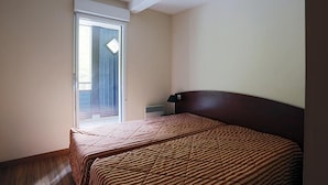A bedroom with a bed, a nightstand, a window, and a door. - 100m from ski slopes, 1st floor, jacuzzi, hammam, parking, tv, ski locker, 41m², Peyragudes (Germ)