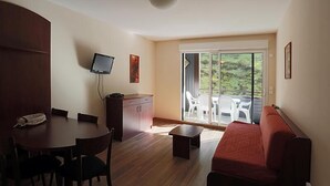 A room with a dining table, chairs, a sofa, a TV, a cabinet, and a sliding glass door to a balcony with chairs. - 100m from ski slopes, 1st floor, jacuzzi, hammam, parking, tv, ski locker, 41m², Peyragudes (Germ)