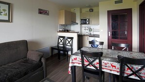 Un espace de vie compact comprenant un canapé, une table à manger avec des chaises, un coin cuisine avec des placards et des appareils électroménagers, et une porte rouge.