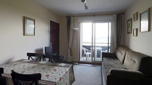 Une pièce comprenant une table à manger, des chaises, un canapé, un téléviseur et une porte-fenêtre coulissante donnant sur un espace extérieur.