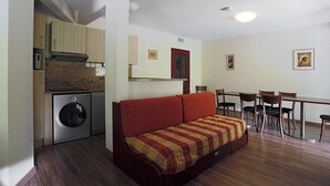 A compact room with a bed, a dining table, chairs, a small kitchen area with a washing machine, and a red-framed window. - 100m from ski slopes, 2nd floor, view ski slopes, jacuzzi, hammam, parking, tv, ski locker, 66m² (Germ)
